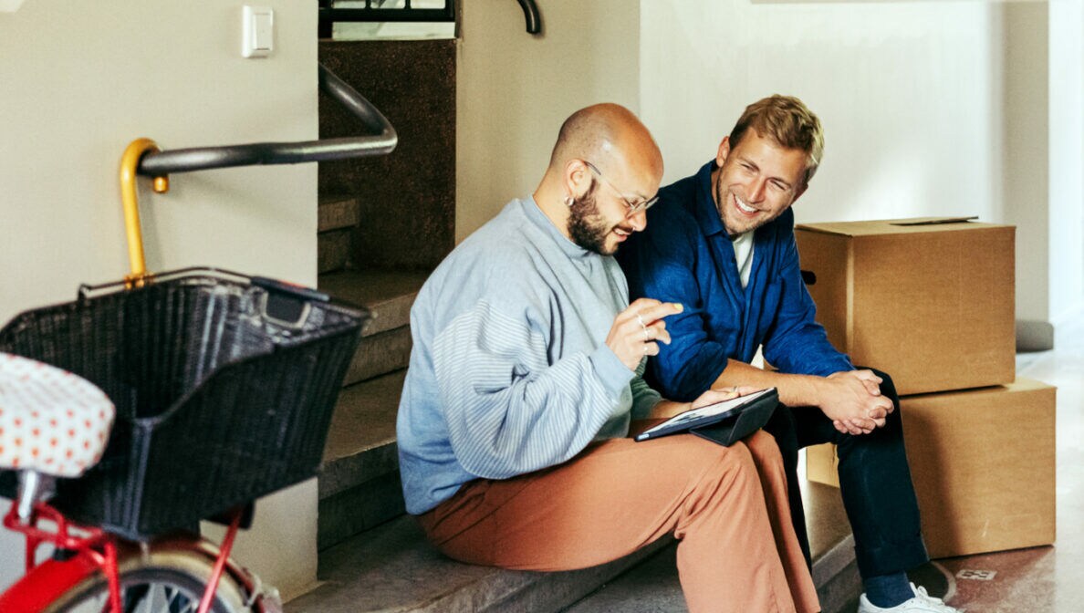 Zwei Personen sitzen am Ende einer Treppe auf den Stufen und schauen auf ein Tablet.