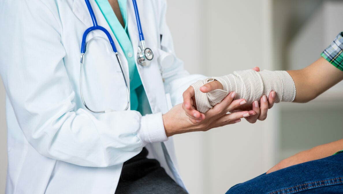 Nahaufnahme eines Arztes, der einen einbandagierten Arm untersucht.