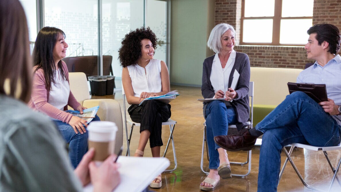 Mehrere Personen sitzen gemeinsam in einer Art Stuhlkreis und unterhalten sich.