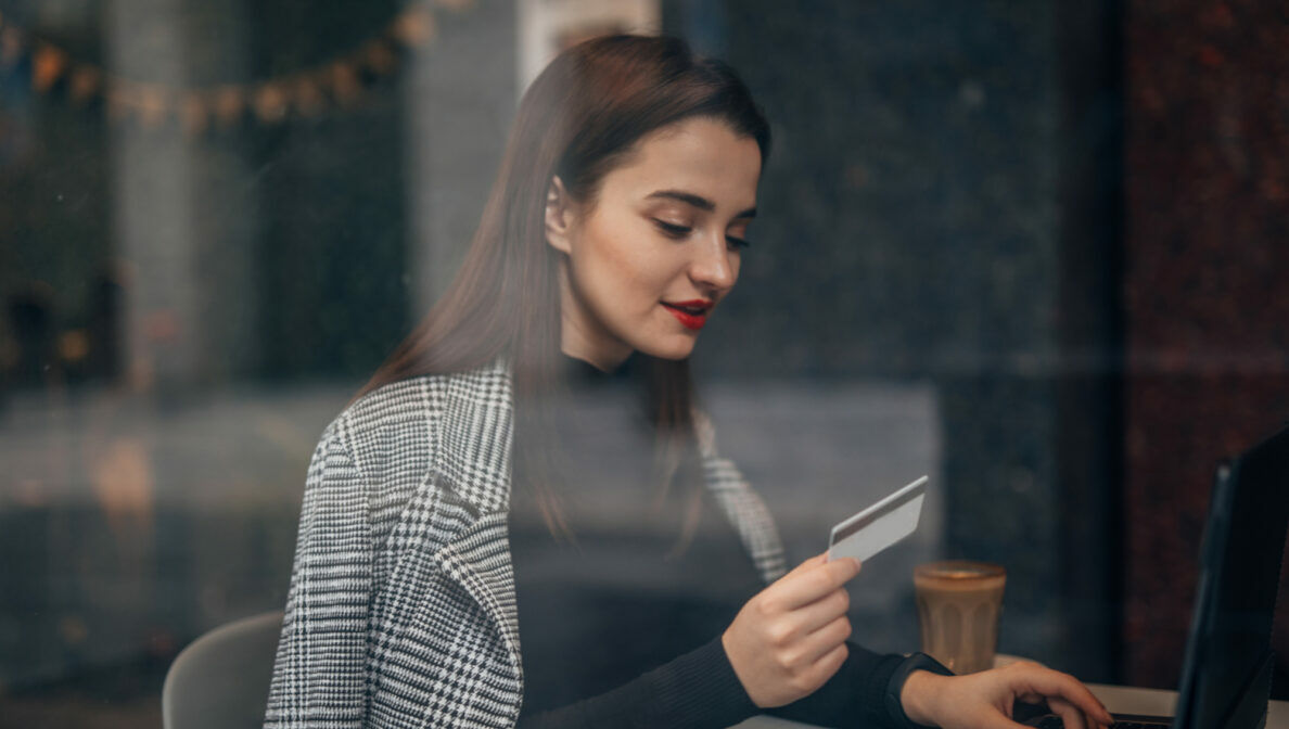 Eine Person sitzt vor einem geöffneten Laptop und hält eine Bankkarte in der Hand.