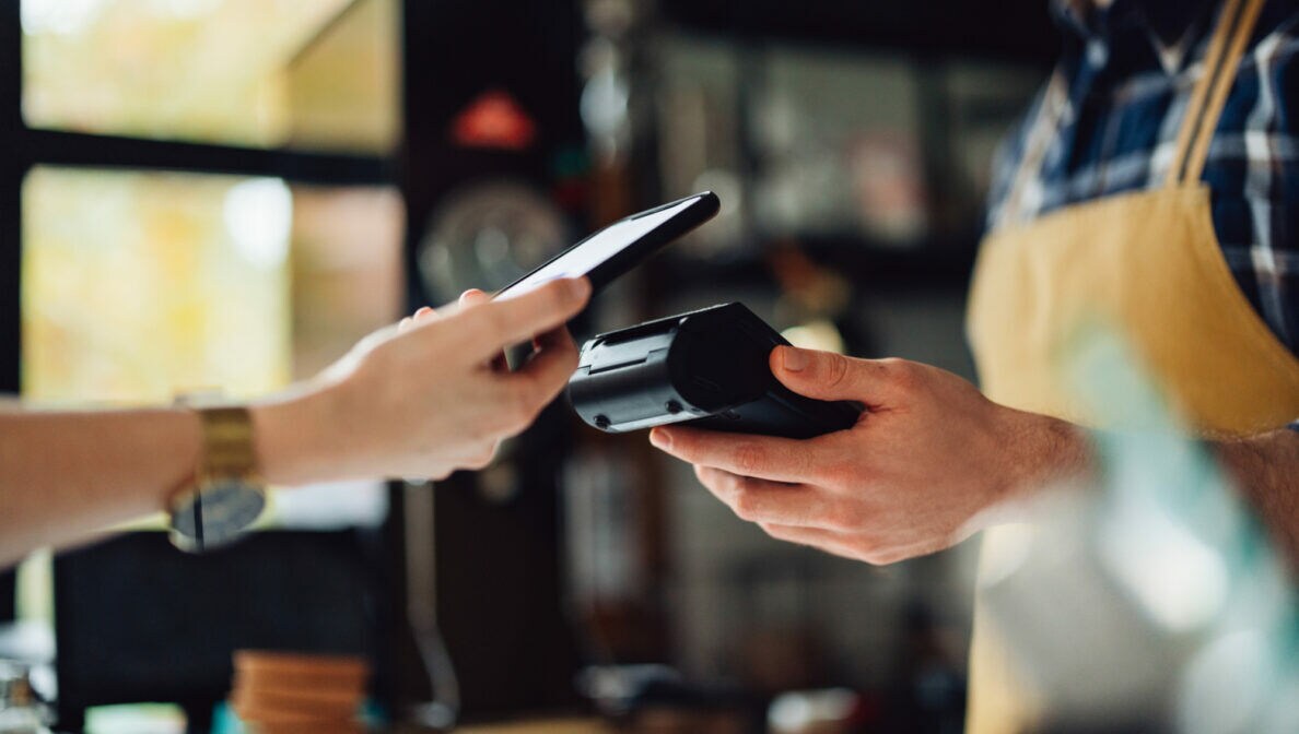 Eine Person bezahlt mit dem Smartphone kontaktlos an einem Terminal.