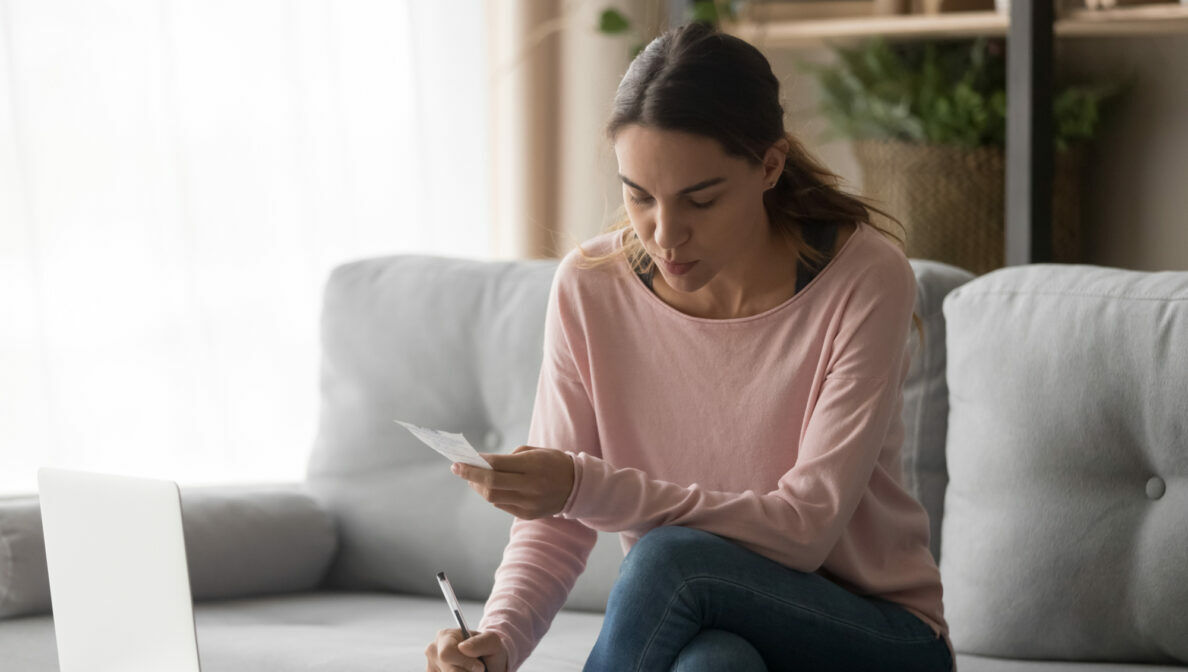 Eine Person sitzt auf einem Sofa und trägt etwas auf einem Blatt Papier ein.