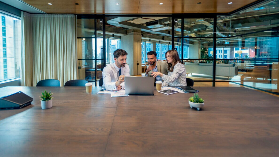 Mehrere Personen sitzen in einem Büroumfeld zusammen vor einem Laptop.