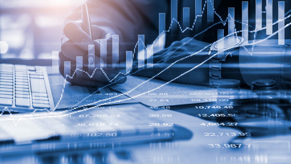 Aktienchart mit technischen Indikatoren, im Hintergrund eine Nahaufnahme einer Person am Schreibtisch.