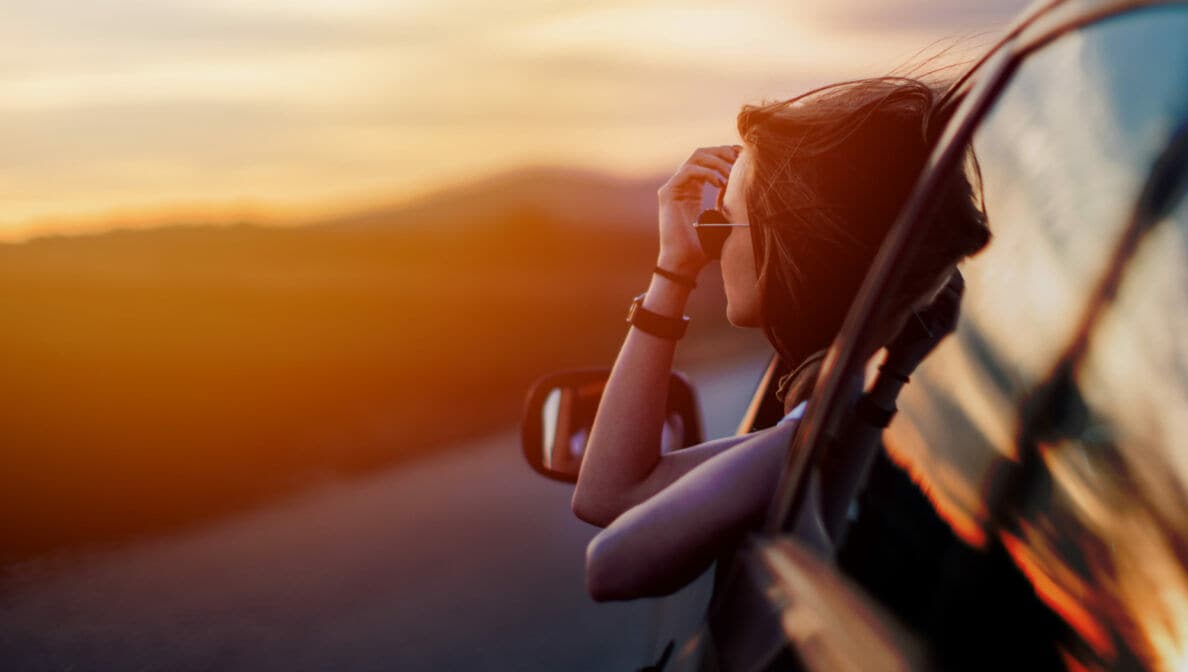 Eine Person lehnt sich in der Abendsonne aus dem Fenster eines Autos.