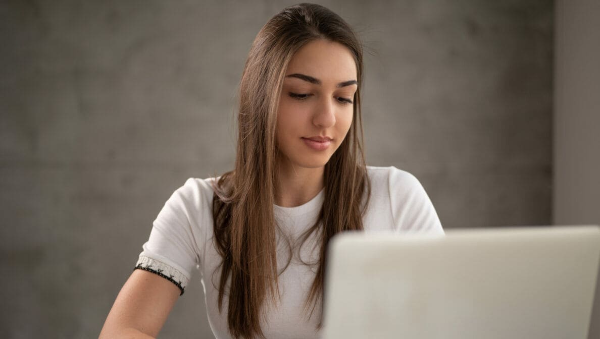 Eine junge Frau sitzt vor einem aufgeklappten Laptop.