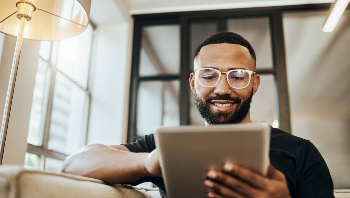 Ein Mann sitzt auf einem Sofa und hält ein Tablet in der Hand.