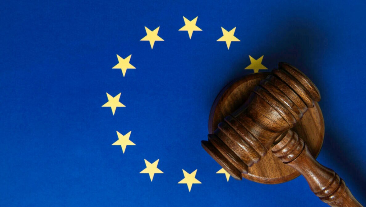 Ein Hammer, wie ihn zum Beispiel in amerikanischen Filmen Richter zur Urteilsverkündung nutzen, liegt mit einem passenden Gegenstück auf einer europäischen Flagge in blau mit gelben Sternen.