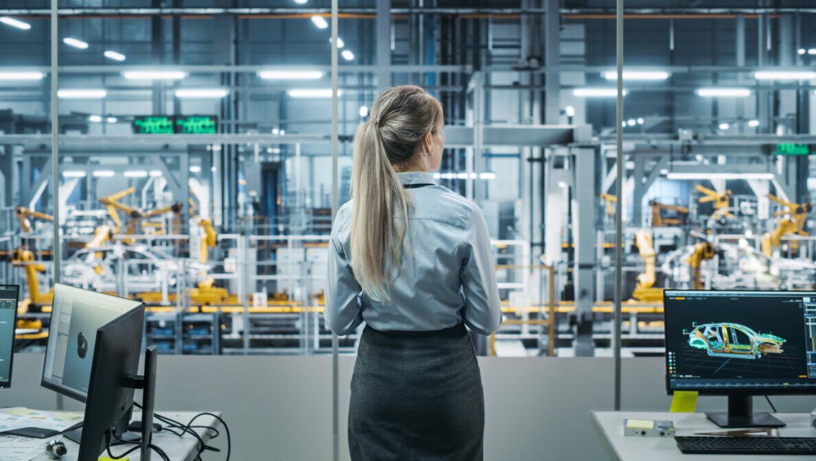 Eine Person blickt durch eine Glaswand auf eine durch Roboter gesteuerte Fertigungskette.