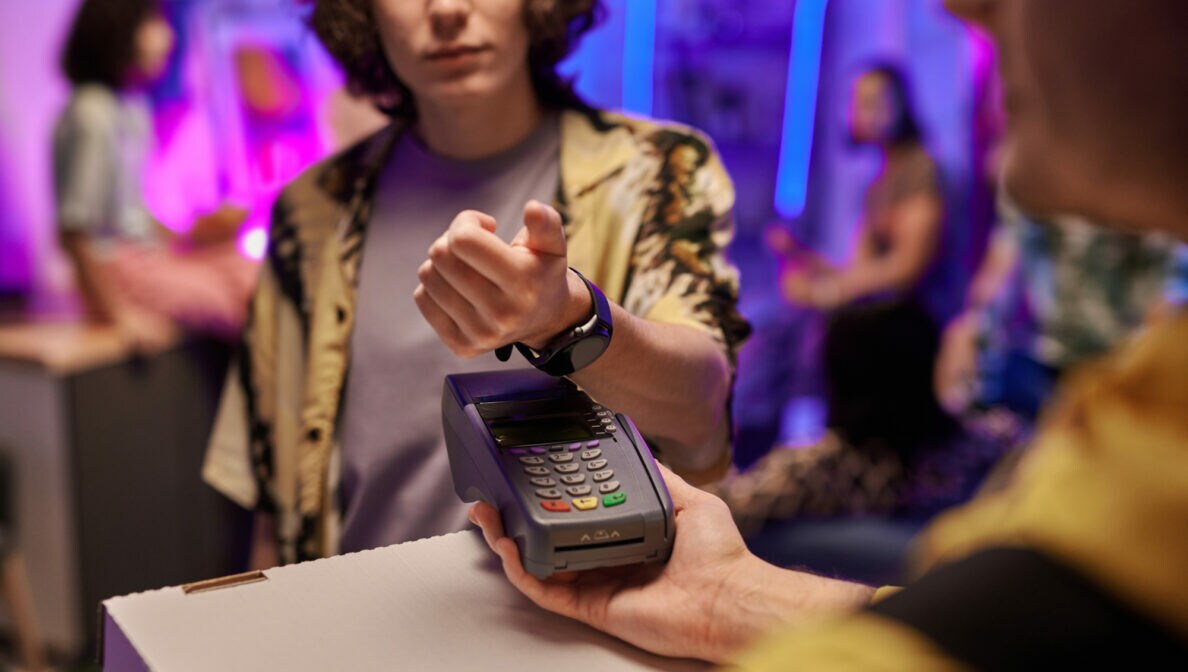 Eine Person hält die Smartwatch an ihrem Arm über ein Zahlungsgerät, das eine ihr hinhält.