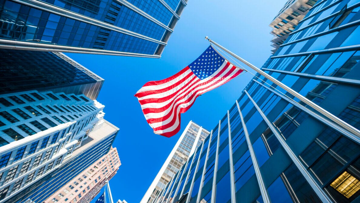 Die US-amerikanische Flagge weht zwischen hohen Bürogebäuden.