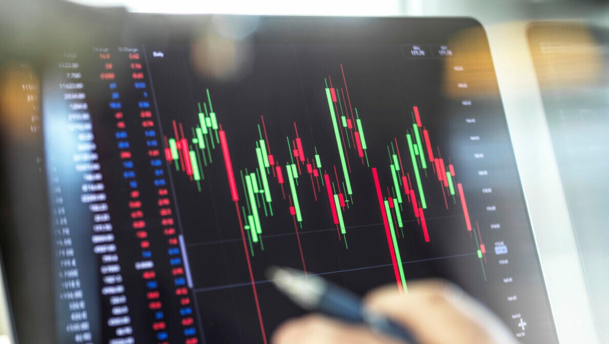 Eine Person zeigt mit dem Finger auf einen Bildschirm, auf dem Kurven, Zahlen und Prozentangaben abgebildet sind.