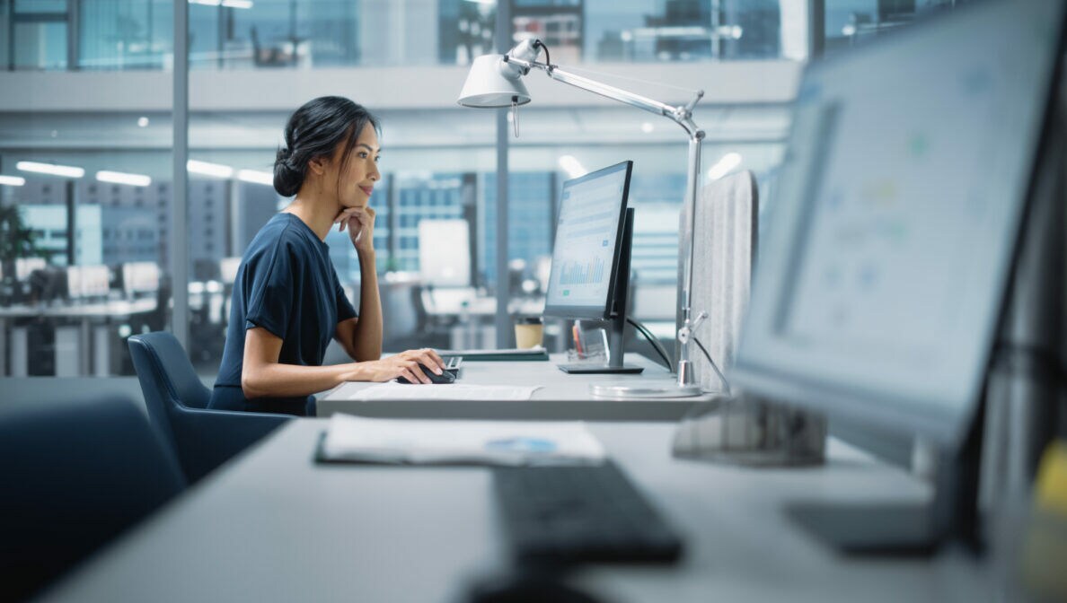Eine junge Frau sitzt in einem Büro an einem Tisch mit Computer.
