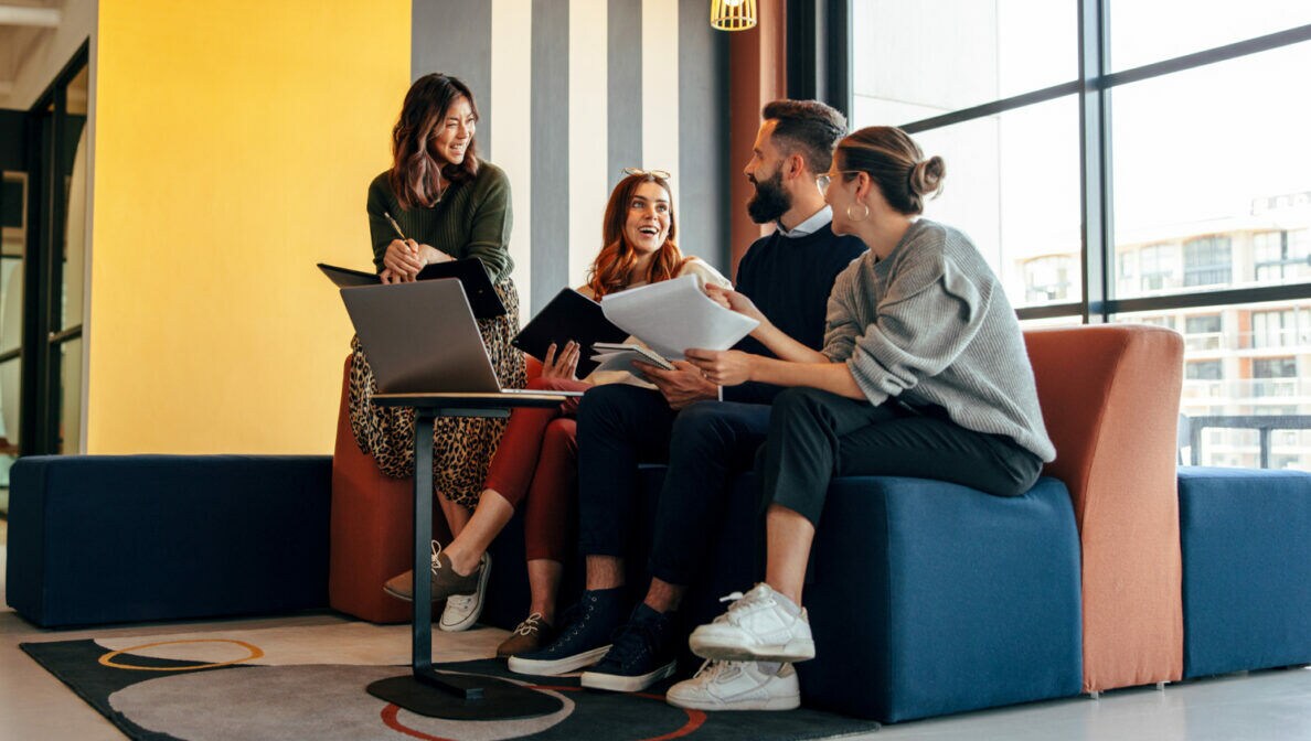 Mehrere Personen sitzen in einem loftartigen Büro zusammen auf einer Couch.