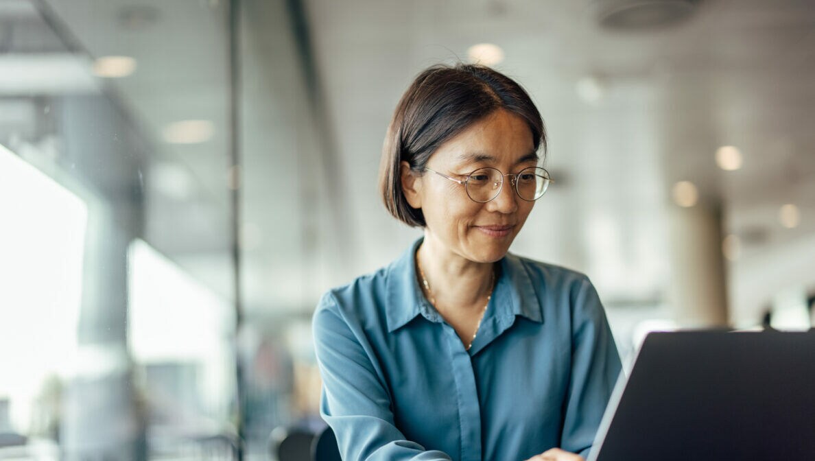 Eine Person sitzt lächelnd vor einem Laptop am Tisch.