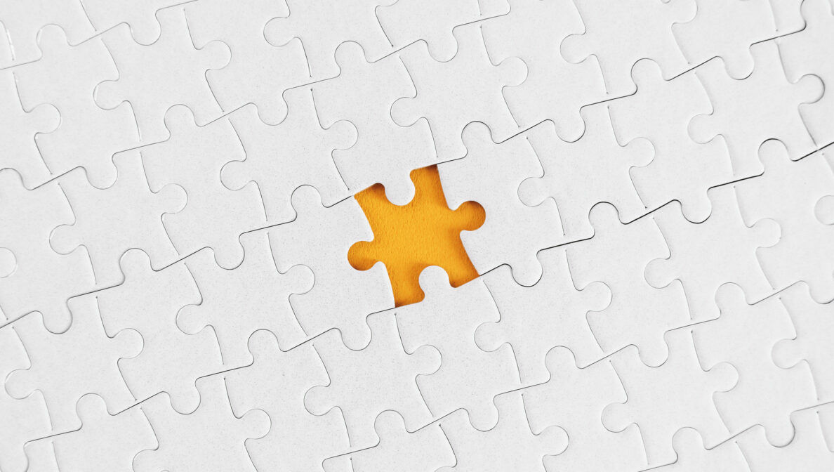 Ein weißes Puzzle, bei dem ein Teil fehlt. Dahinter ist eine gelbe Oberfläche zu sehen.