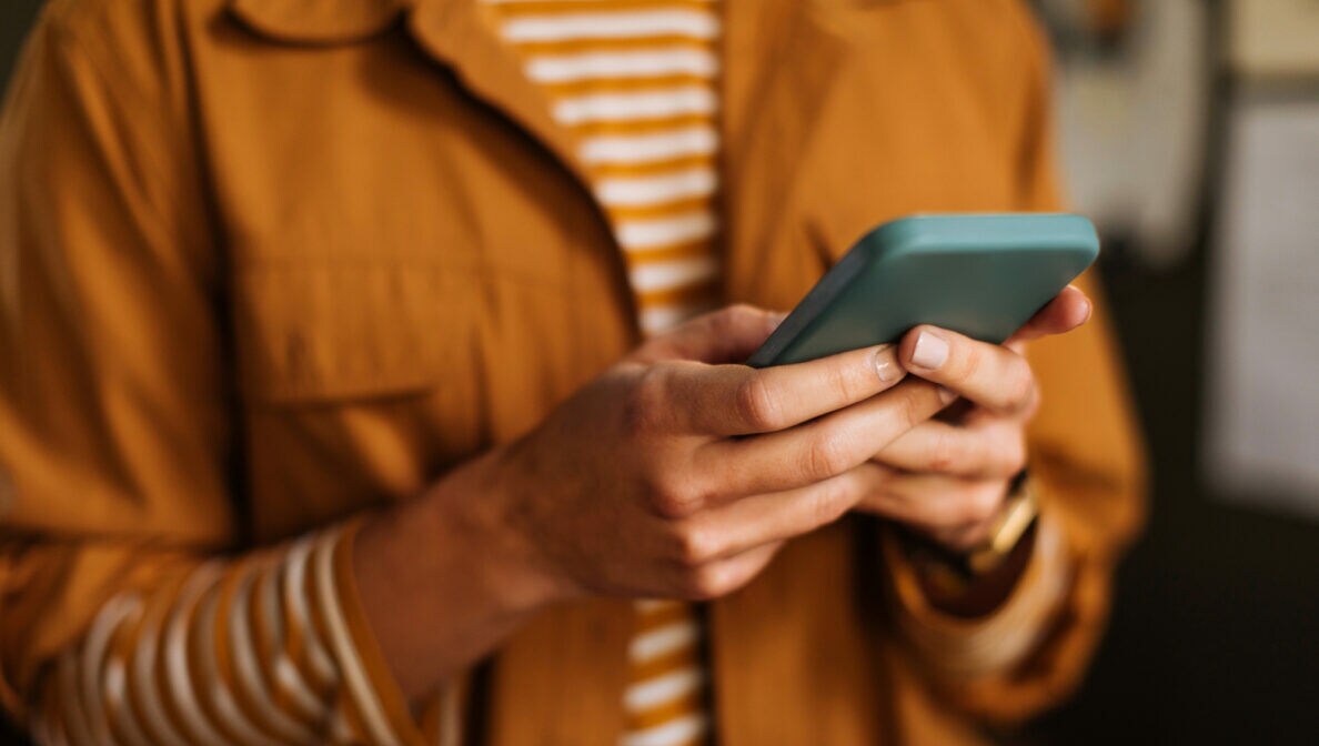 Eine Person hält mit beiden Händen ein Smartphone auf Brusthöhe.