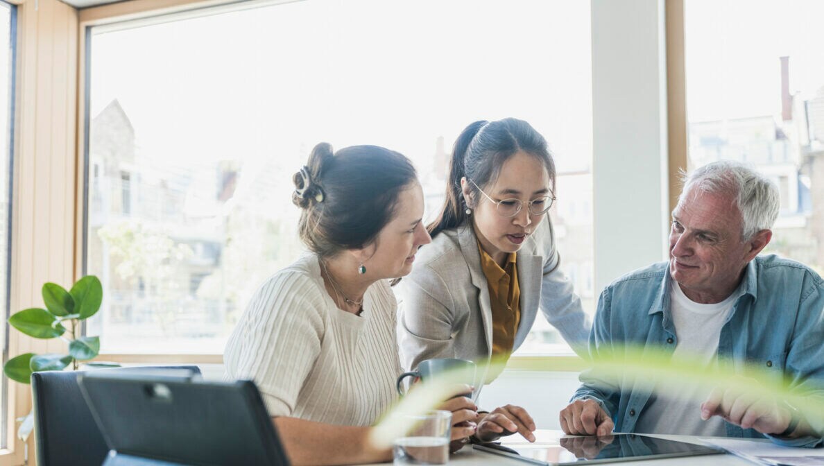 Drei Personen sind im Gespräch und haben ein Tablet auf dem Tisch vor ihnen liegen.