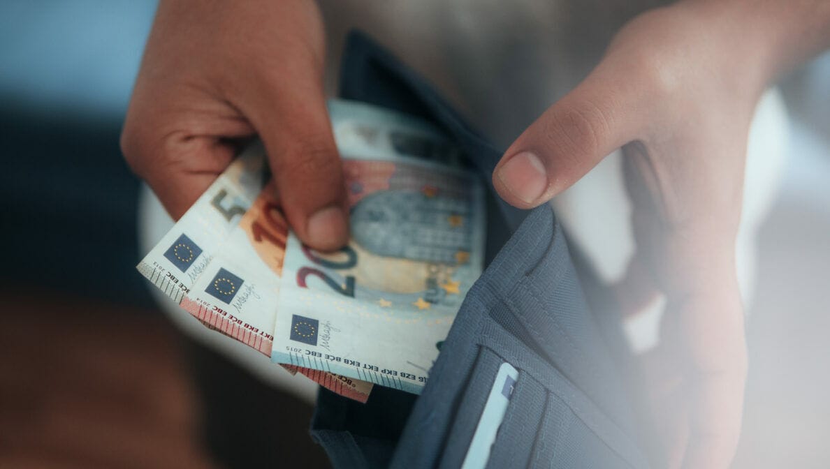 Eine Person nimmt Geldscheine aus einem Portemonnaie .