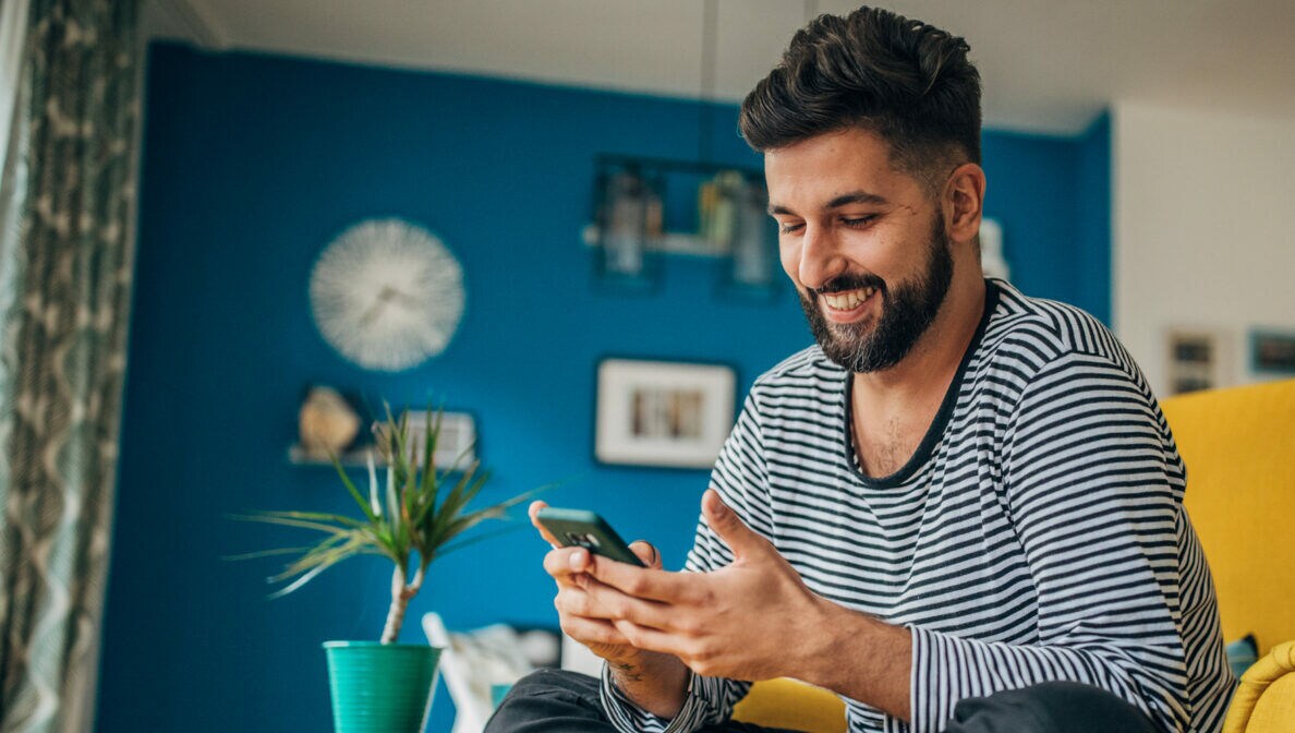 Eine Person sitzt im Schneidersitzt auf einem Sessel und blick auf das Smartphone in ihren Händen.
