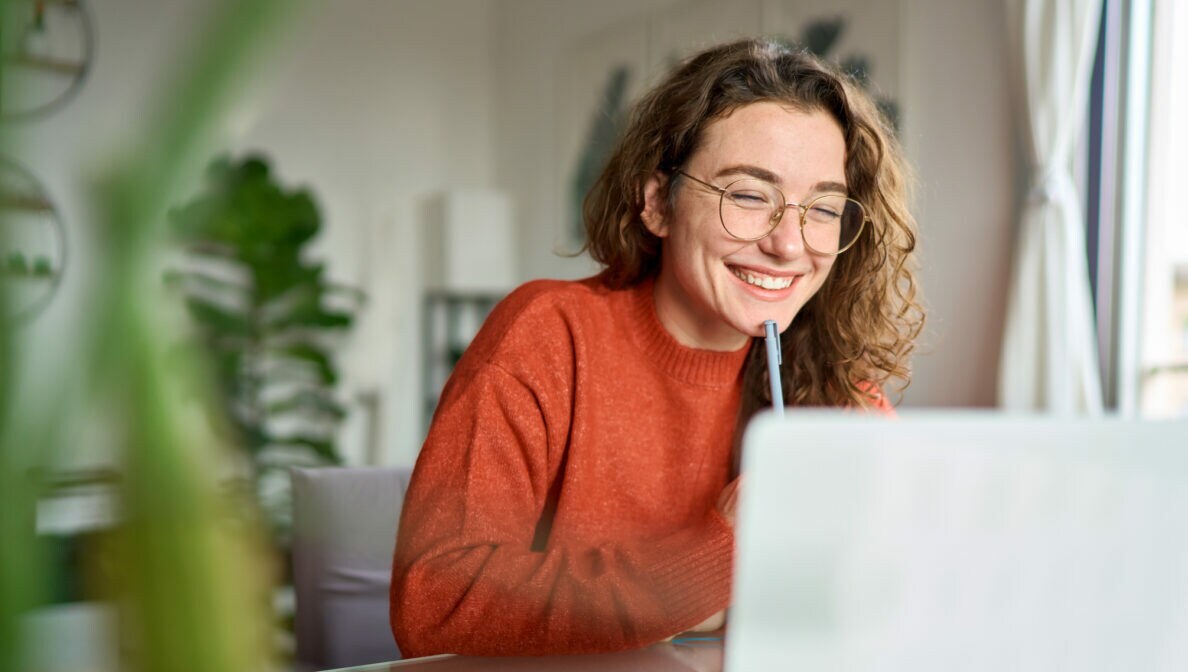 Eine Person sitzt vor einem geöffneten Laptop, daneben liegt ein Smartphone.