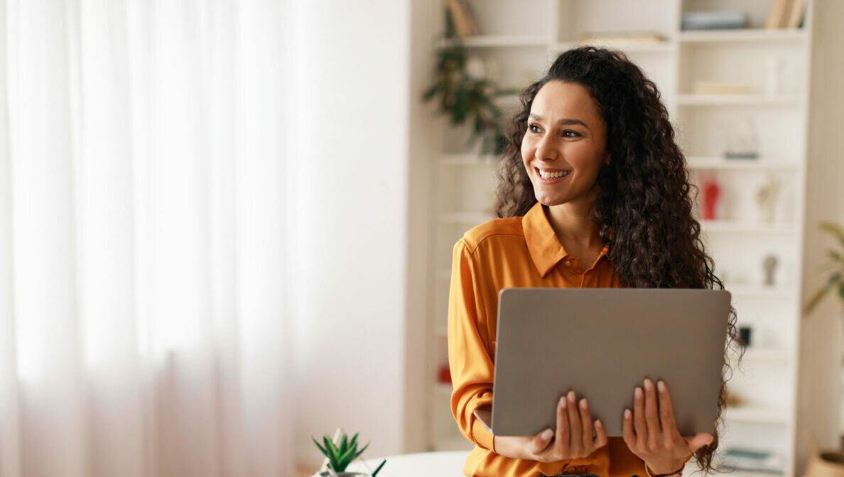 Eine Person lehnt an einem runden Tisch und hält ein geöffnetes Notebook in den Händen.