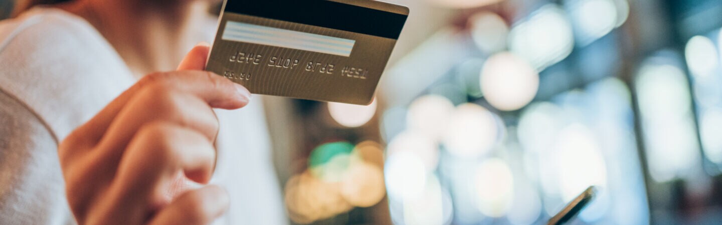 Eine lachende Frau hält ihr Smartphone und eine goldene Kreditkarte in ihren Händen