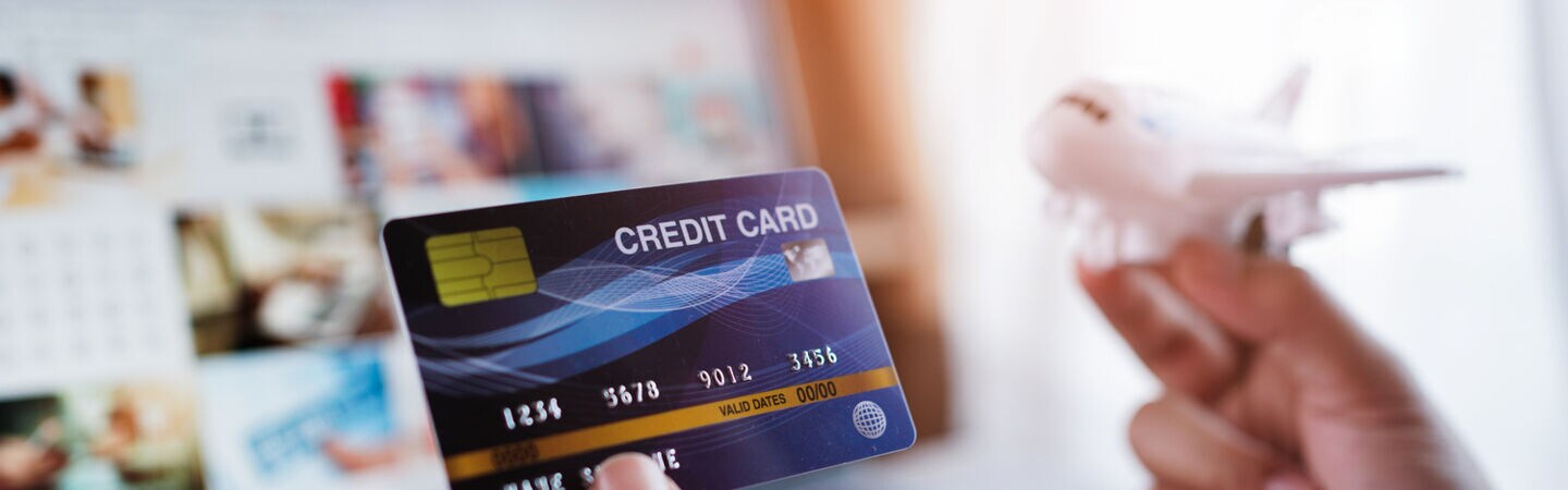 Zwei Hände, eine Kreditkarte und ein Flugzeugmodell haltend, vor einem Laptopbildschirm