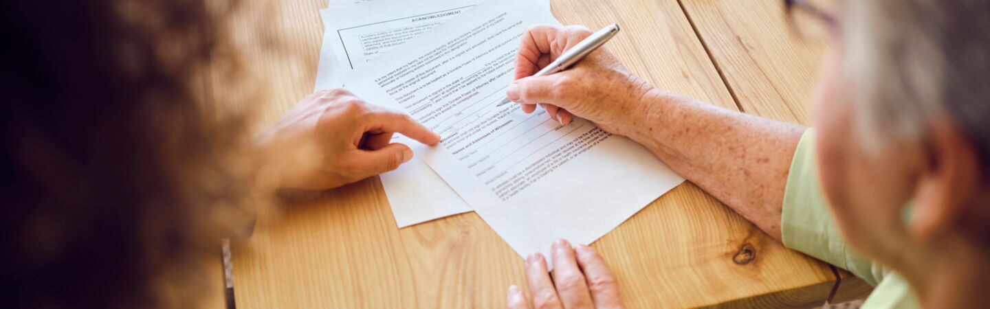 Zwei Personen an einem Tisch, von denen eine Dokumente unterzeichnet