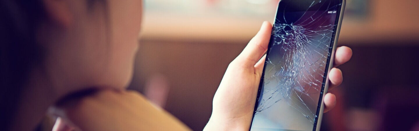 Eine Person betrachtet das Display ihres Smartphones, das zersprungen ist.