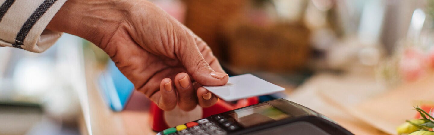 Eine Person hält eine Karte zum Bezahlen an ein Kartenlesegerät.