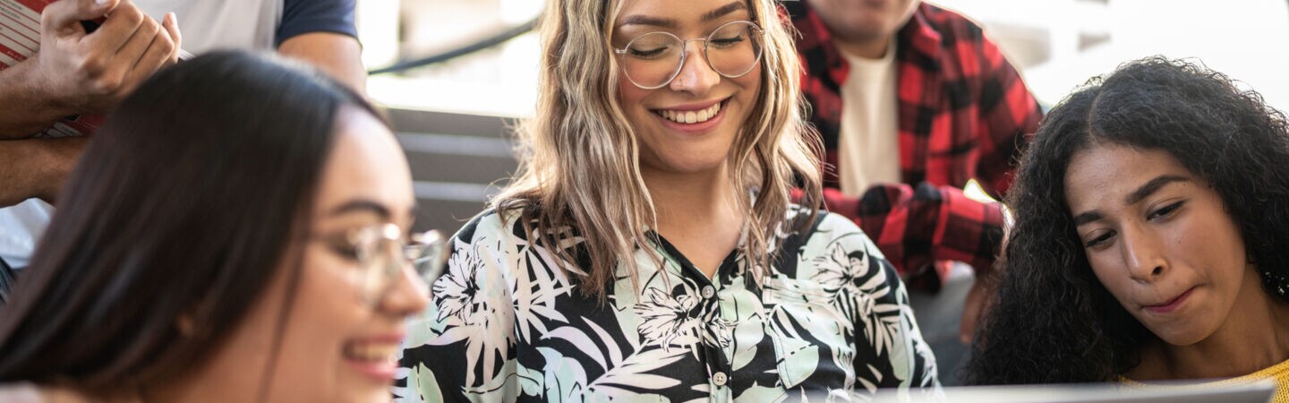 Mehrere junge Personen sitzen in einem Hörsaal um ein Laptop herum.