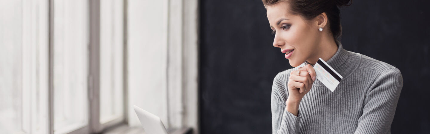 Eine Frau sitzt vor einem Laptop und hält eine Bankkarte in der Hand.