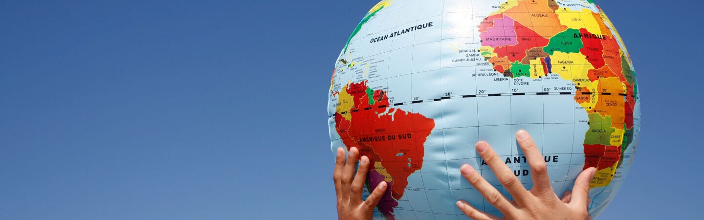 Mehrere Hände halten einen Ball mit Weltkugelmotiv in die Höhe.