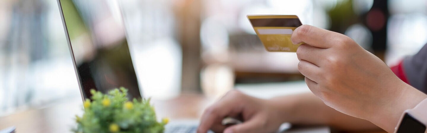 Nahaufnahme einer Hand, die eine Bankkarte hält, die andere Hand liegt auf einer Laptoptastatur.