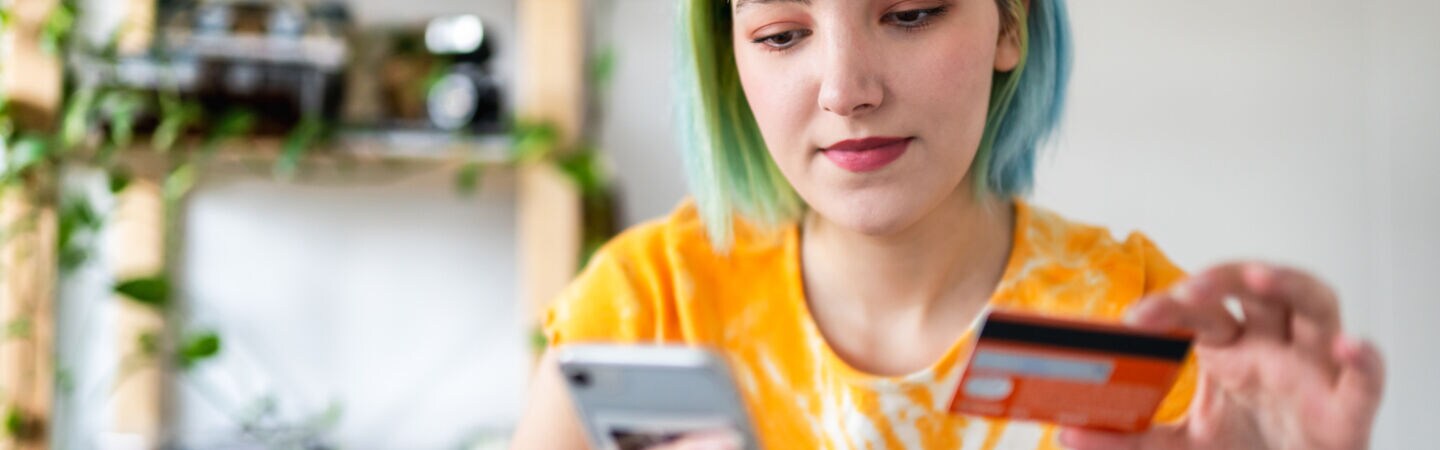 Nahaufnahme einer Person, die ein Smartphone sowie eine Bankkarte in den Händen hält.