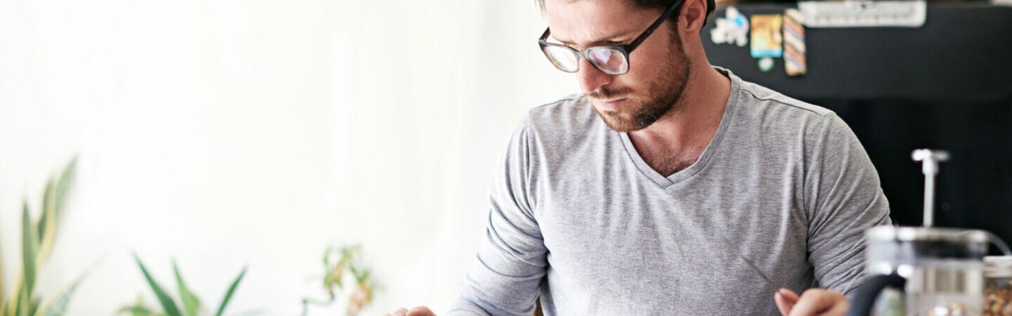 Eine Person sitzt am Frühstückstisch und tippt auf ihr Tablet.