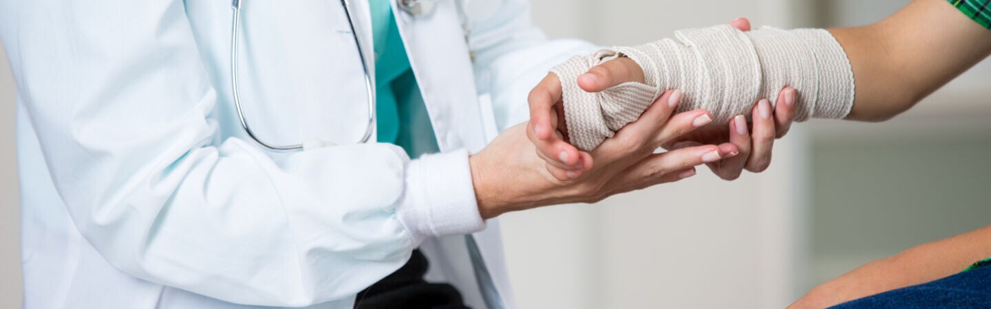 Nahaufnahme eines Arztes, der einen einbandagierten Arm untersucht.