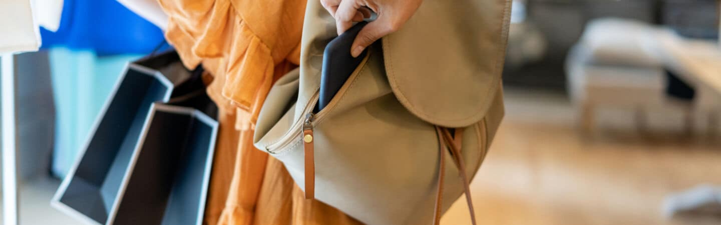 Nahaufnahme einer Hand, die ein Smartphone aus einem Rucksack entwendet.