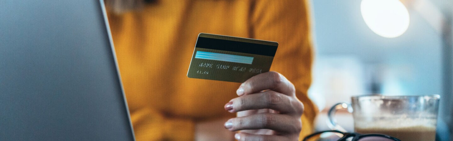 Nahaufnahme einer Person, die vor einem Laptop sitzt und eine Kreditkarte in der Hand hält.