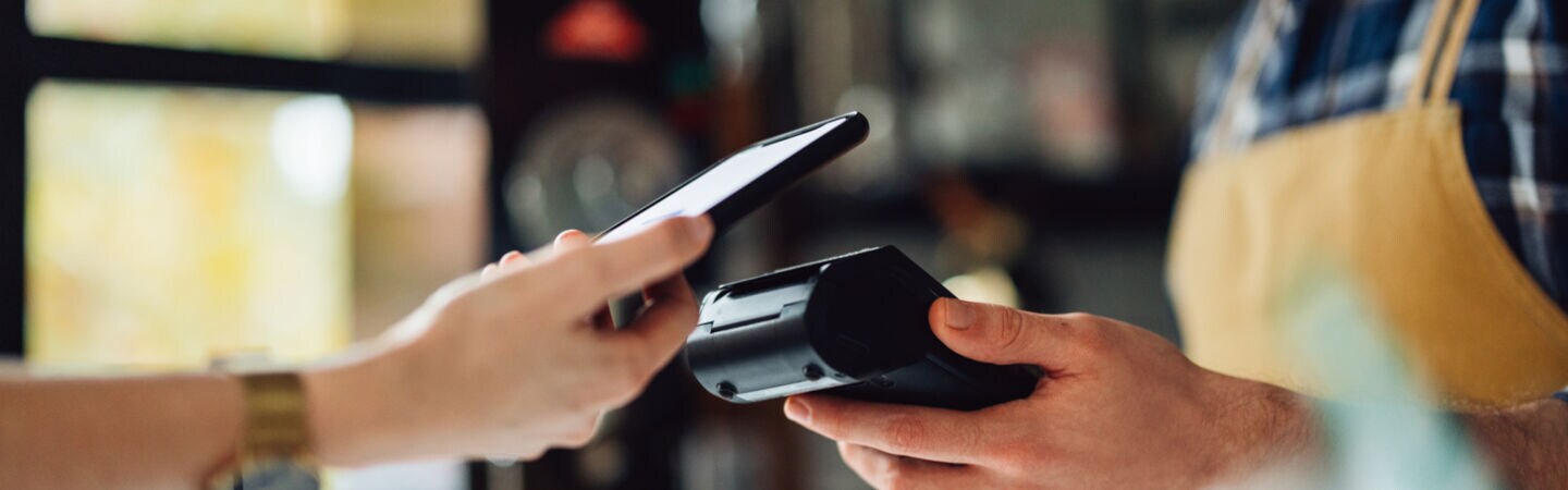 Eine Person bezahlt mit dem Smartphone kontaktlos an einem Terminal.