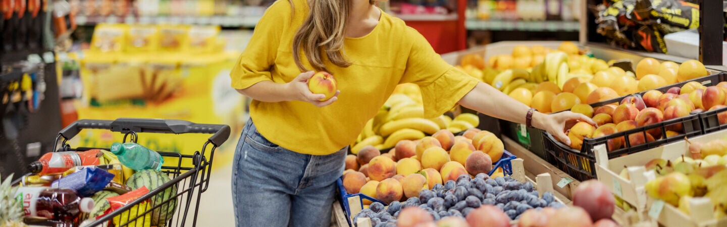 Eine Person greift im Supermarkt nach Pfirsichen.