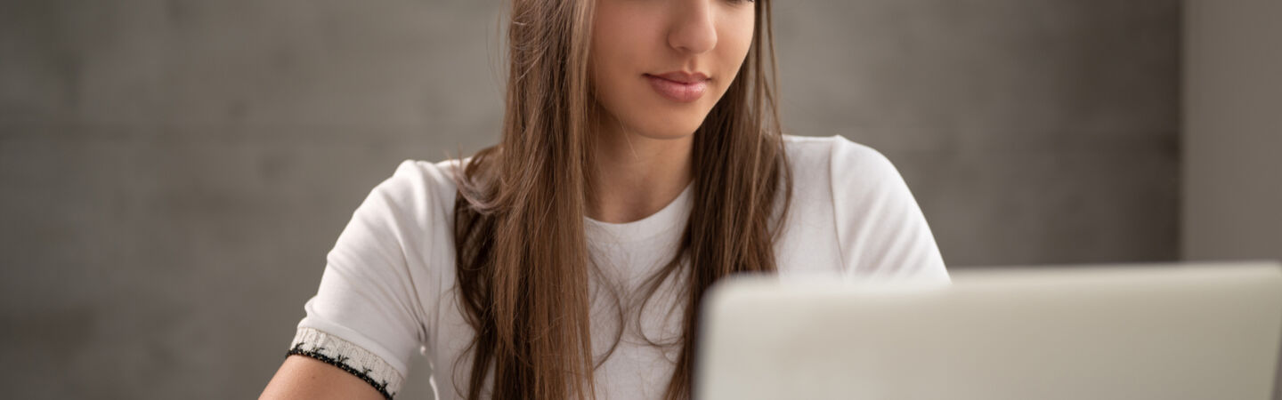 Eine junge Frau sitzt vor einem aufgeklappten Laptop.