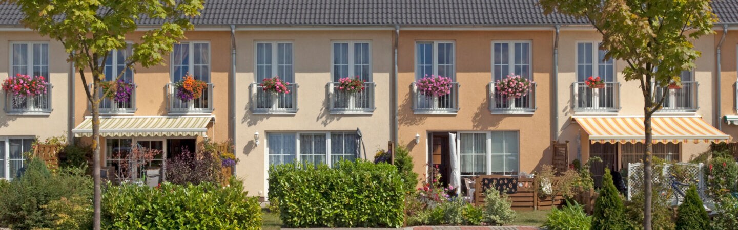 Hellgelb verputzte Reihenhäuser mit weißen Fenstern und Türrahmen.