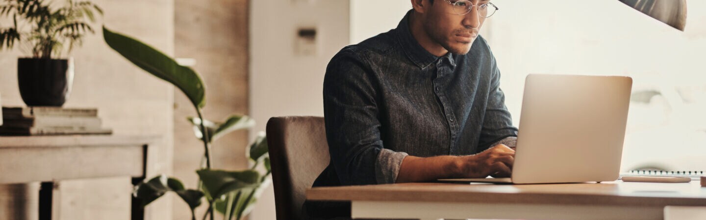 Eine Person sitzt vor einem geöffneten Laptop am Tisch.