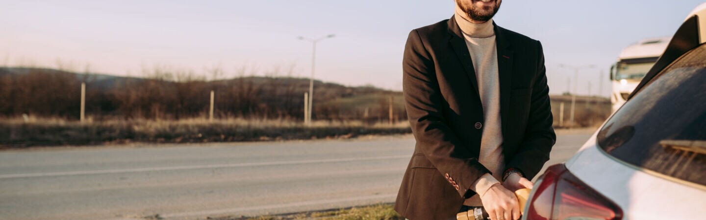 Eine Person steht vor ihrem Auto und hält den Zapfhahn fest, der im Auto steckt.