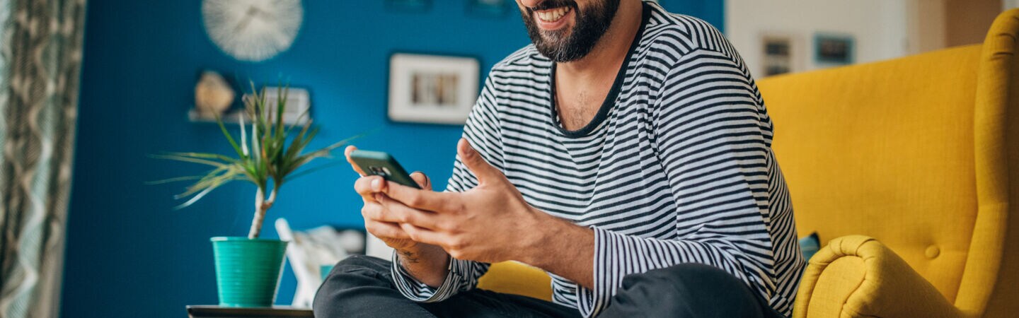 Eine Person sitzt im Schneidersitzt auf einem Sessel und blick auf das Smartphone in ihren Händen.