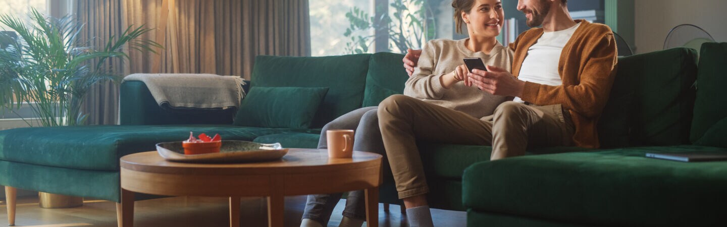 Zwei Personen sitzen nebeneinander auf einem Sofa und blicken gemeinsam auf ein Smartphone.