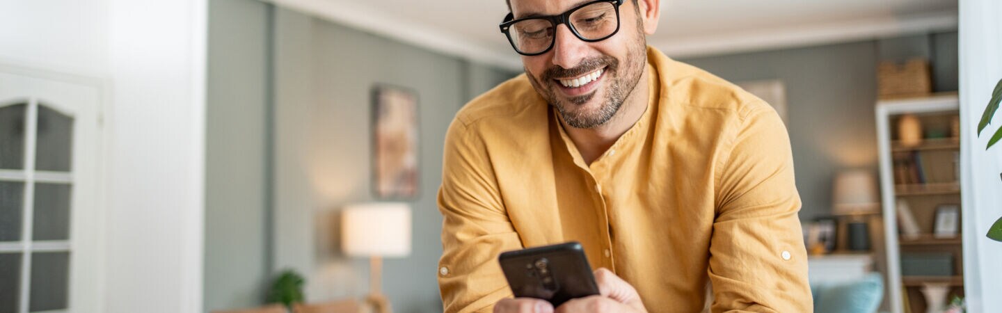 Eine Person lehnt auf einer Kücheninsel und blickt lächelnd auf das Smartphone in ihren Händen.