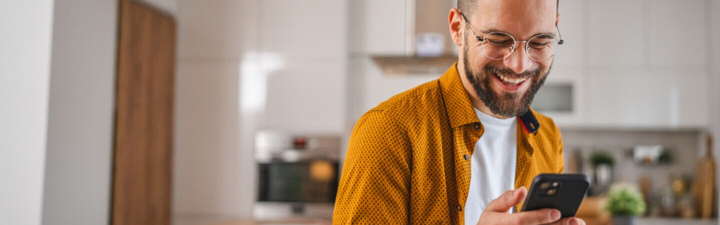 Eine Person hält ein Smartphone in den Händen und blickt lächelnd drauf.